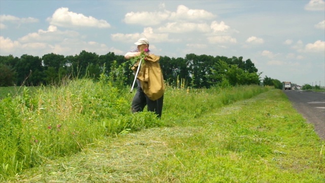 在夏天的时候，一位年长的乌克兰农民拄着拐杖背着沉重的袋子在路边行走视频下载