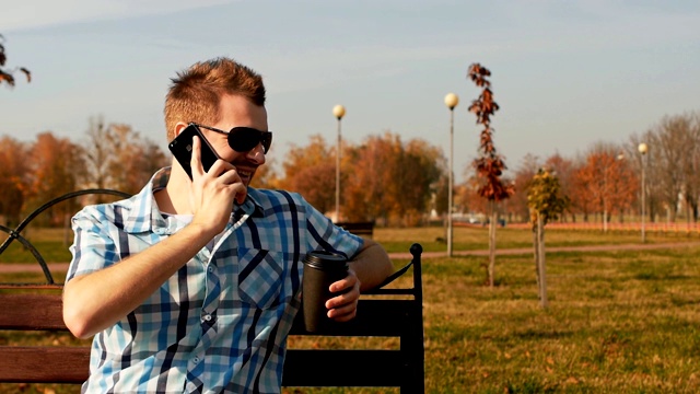 一个留着胡子的家伙，端着一杯咖啡坐在长凳上打电话视频素材