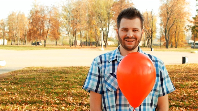 满脸胡子的男人站在那里，手里拿着一个红色的气球视频下载