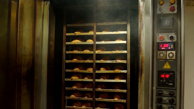 一位女性甜品师打开烤箱，里面放着新鲜的糕点和羊角面包。糖果和烘焙制造业，慢镜头视频下载
