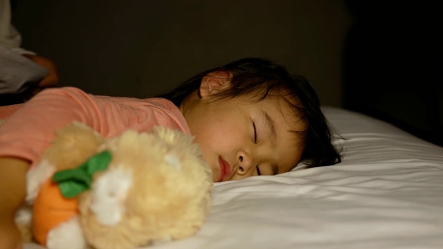 亚洲母亲给睡在床上的女儿盖上毯子，然后用爱吻她。卫生保健的概念。视频下载