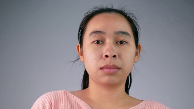 年轻的亚洲女人与哈欠的表情在灰色的背景。视频下载