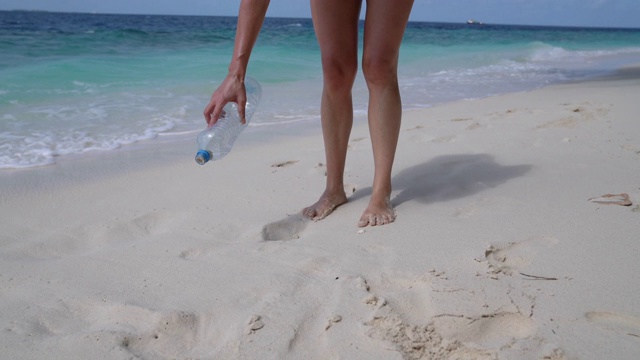 一个年轻的成年女子在海滩上捡一些废弃的塑料瓶视频下载