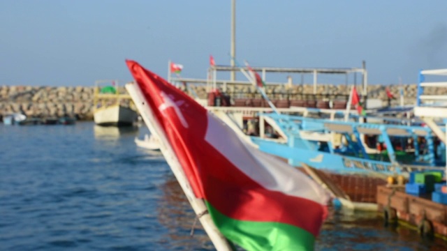阿曼的穆萨丹姆飘扬着阿曼的国旗，度假的阿曼人乘坐单桅帆船穿过峡湾、岩石山脉和中东霍尔木兹海峡附近的蓝色海水。视频下载