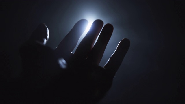 一个人的手伸向光，手指玩弄着光并经过光源。宗教、灵性和魔法概念。视频素材