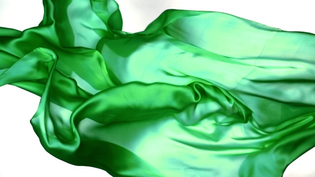金属绿色丝质织物在超慢的动作中横向流动和摆动，近距离，白色背景视频素材