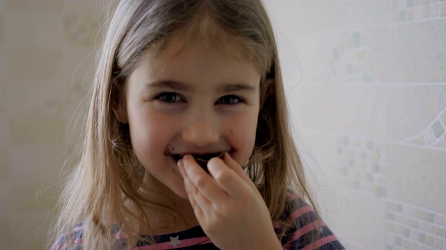 小女孩被巧克力弄脏了。有趣的脸。肮脏的小女孩在吃巧克力。吃甜点后的余味视频素材
