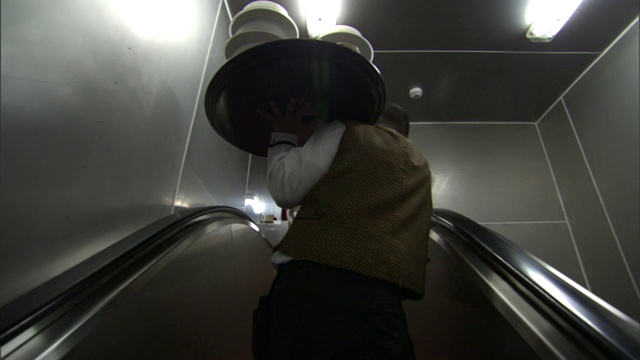 一名侍者端着一盘菜，用自动扶梯向餐厅走去。视频素材