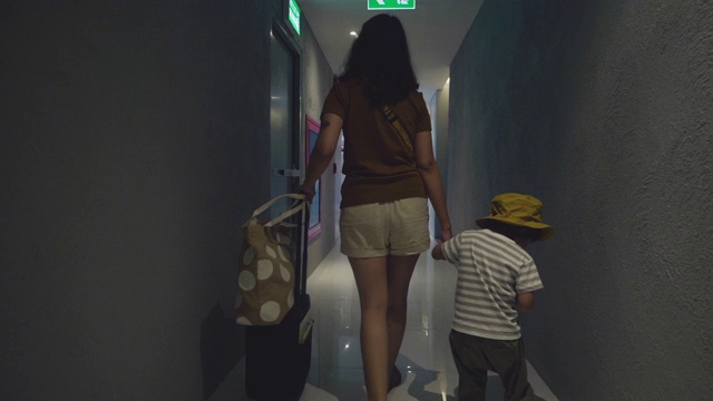 亚洲母亲和她的儿子拉着手提箱在酒店走廊。视频下载