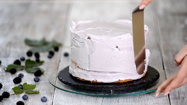 糖果商用烹饪抹刀将紫色奶油抹在饼干蛋糕上。自制糕点的概念，烹饪蛋糕。视频下载