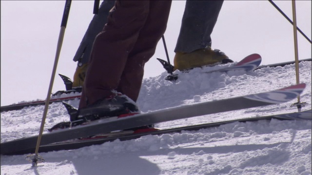 三个滑雪者在一个多雪的斜坡顶上等着。视频下载