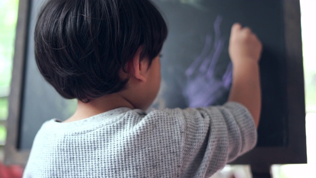 这个男孩用粉笔在黑板上画画。视频素材