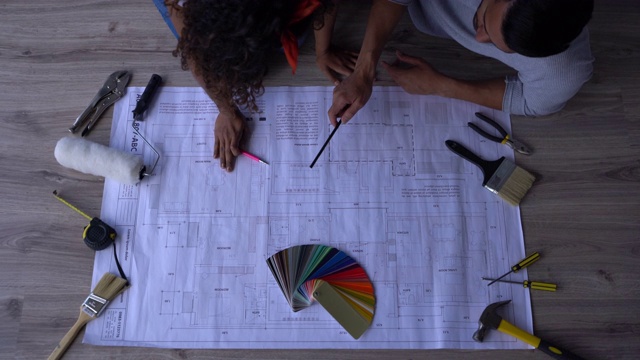 一对拉美夫妇坐在地板上看着他们新家的蓝图做计划视频素材