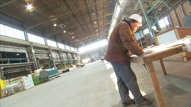 一个戴安全帽的男人在看仓库的建筑设计图。视频下载