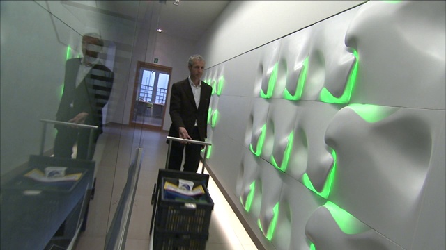 一个男人推着手推车沿着一座现代建筑的走廊走。视频素材