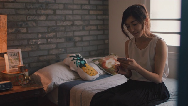 在日本东京，一名妇女坐在/躺在床上用手机打字。视频素材