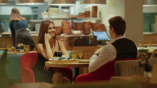 在一家昂贵的现代餐厅里，年轻美丽的女子与一位优雅的男子坐在一张桌子旁。一个美女和一个男人在餐厅约会。视频下载
