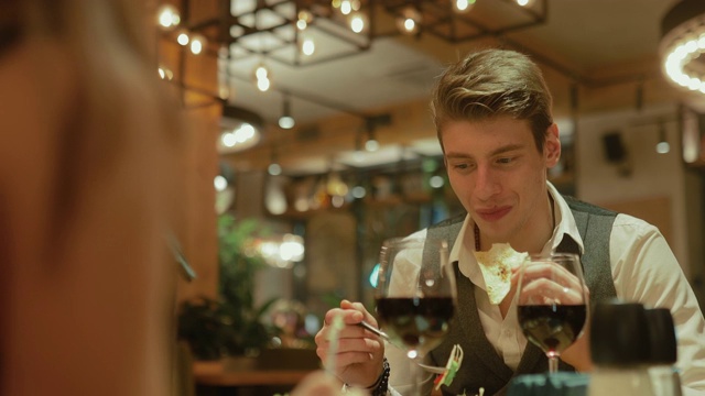 一个快乐的年轻人正在餐馆里吃饭。一瓶酒，玻璃杯，一个男人在舒适的餐厅吃沙拉。肖像的观点。视频下载