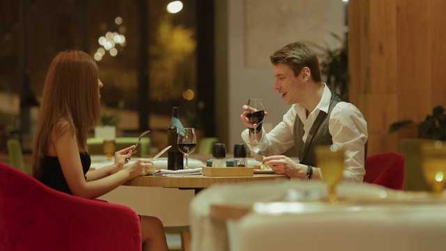 在一家舒适的餐厅里的餐桌。相爱的夫妇坐在一起，吃饭，聊天。相机的侧视图。视频下载
