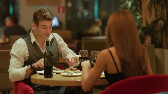 一个年轻英俊的男人和一个漂亮的女人在餐厅吃饭，喝酒。一对夫妇边吃晚饭边聊天。视频下载