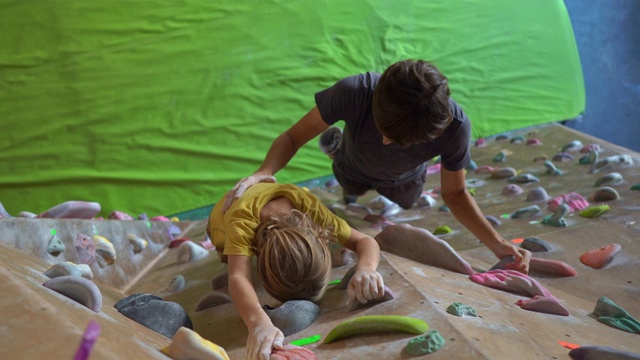 一个年轻的攀岩教练在攀岩馆里教小男孩如何爬墙视频素材