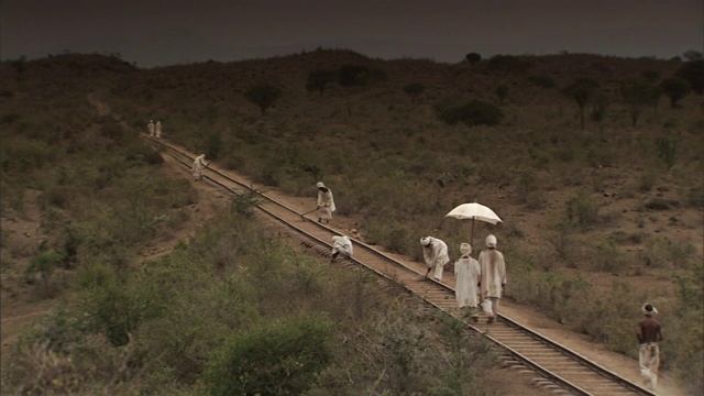 一名男子为另一名男子撑伞，他们沿着一条正在建设的铁路行走。视频素材