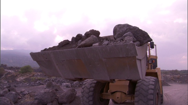 一名重型设备操作员将一车岩石倒入一个大金属箱中。视频素材