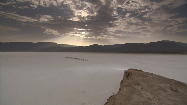 在吉布提的一个盐滩上，云雾笼罩在骆驼队附近的山上。视频素材