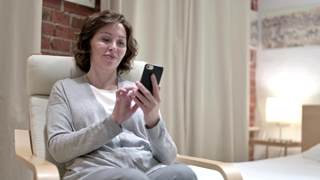 迷人的老女人在卧室里使用智能手机视频素材