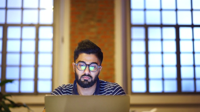 一个年轻人在用笔记本电脑，他的眼镜上有一个网站的映像视频下载
