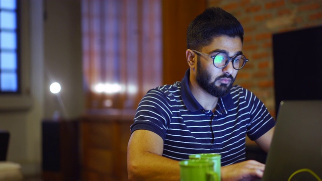 一个年轻人在用笔记本电脑，他的眼镜上有一个网站的映像视频下载