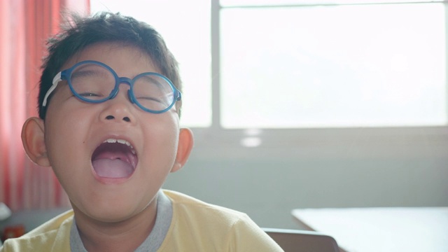 特写的快乐亚洲男孩8岁戴眼镜笑和微笑的房间有阳光从窗户在家里。慢动作视频素材