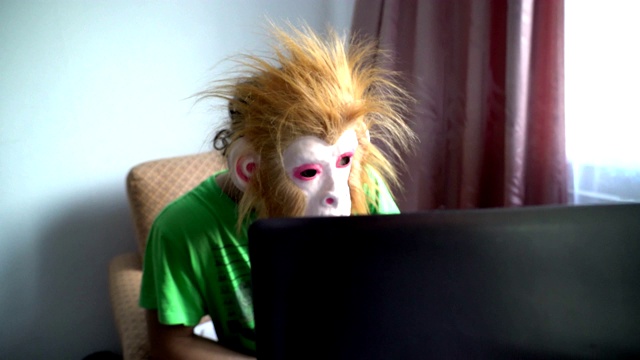 戴着猴子面具的滑稽男人在电脑后面工作。幽默超现实。拖延的概念视频素材