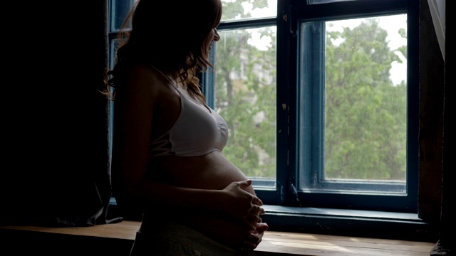 美丽的孕妇站在窗边抚摸着腹部的手视频素材