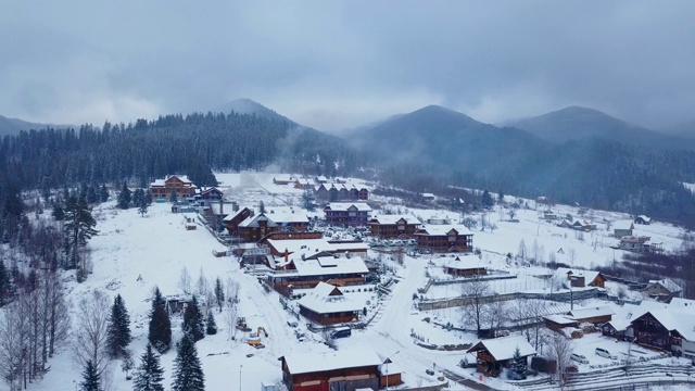冬季山区有人居住地区的空中航拍。山村的建筑物和房屋在雪坡上覆盖着雪。乡村，冷杉和松树林。烟从烟囱视频素材