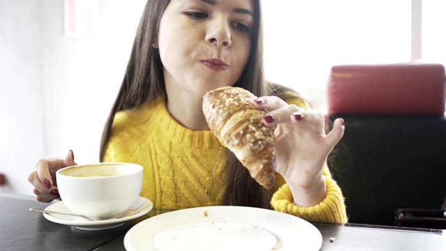 一个女孩在咖啡店里吃着羊角面包。特写镜头。视频素材
