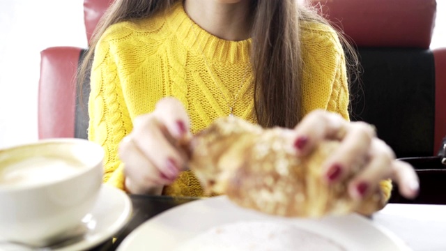 一个女孩在咖啡店里吃着羊角面包。特写镜头。视频素材