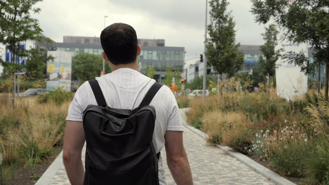 成年白人男子背着背包走在城市户外的街道上视频下载