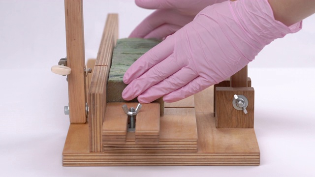 切皂机使用。一根绳子从一块手工肥皂上剪下一块长方形的东西。特写的女性手在粉红色的手套，采取了一个切割片。视频素材