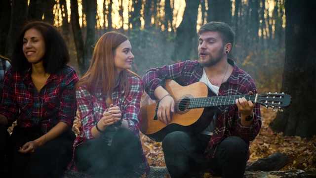 在秋天的森林里，快乐的游客在篝火旁弹吉他视频素材