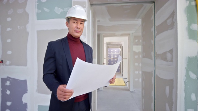 一名男性建筑师站在大楼里，手里拿着平面图，面带微笑视频素材