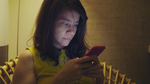 年轻的亚洲女性在卧室里使用手机视频下载