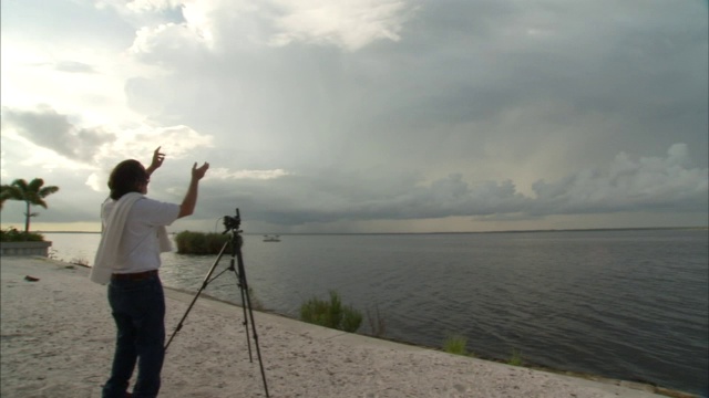 一名科学家将测量装置指向悬挂在河流上方的灰色风暴云。视频下载