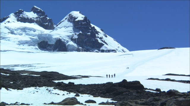 一队徒步旅行者艰难地走下白雪覆盖的山坡。视频下载