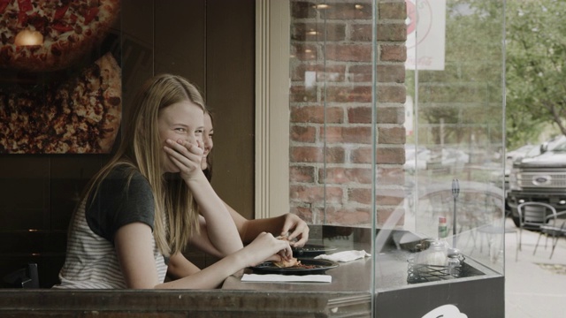美国犹他州普罗沃，一个女孩在人行道上向正在吃披萨的朋友伸出舌头视频素材