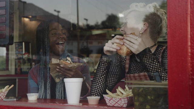 美国犹他州普罗沃，一个女孩在咖啡馆窗口偷偷地吃着朋友的三明治视频素材