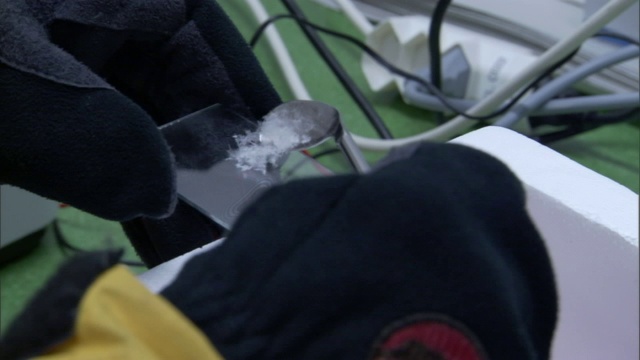 戴着手套的手将雪样本放在载玻片上，然后放到显微镜台上。视频素材