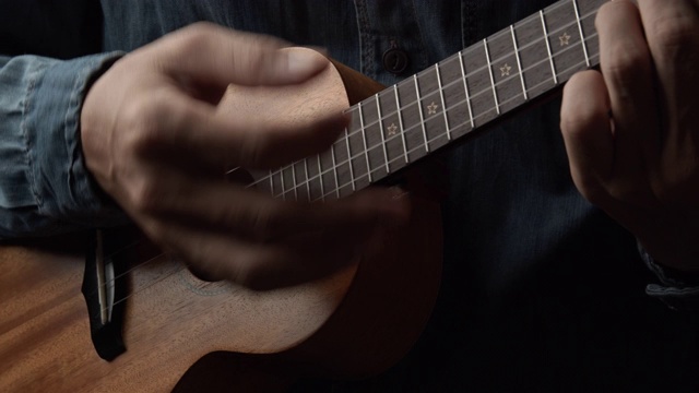 近距离的音乐家男子演奏尤克里里在黑色的背景视频下载