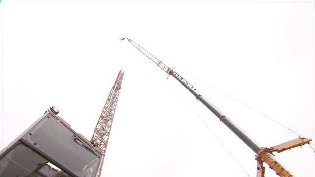 一台巨大的起重机将一位建筑工人吊离地面。视频素材