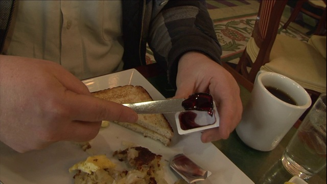 餐馆里，一名男子在吃早餐时把果冻涂在吐司上。视频素材
